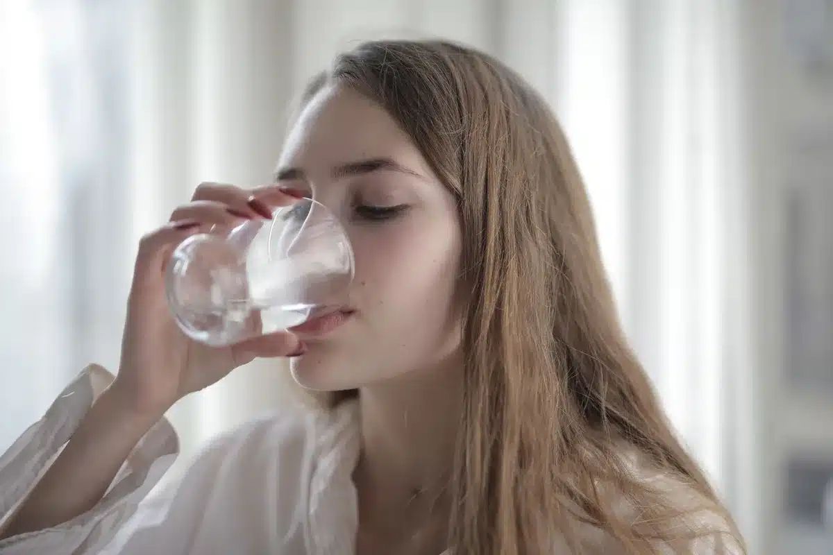 Verre d'eau claire tenu à la main dans une lumière naturelle, symbolisant l'hydratation quotidienne.