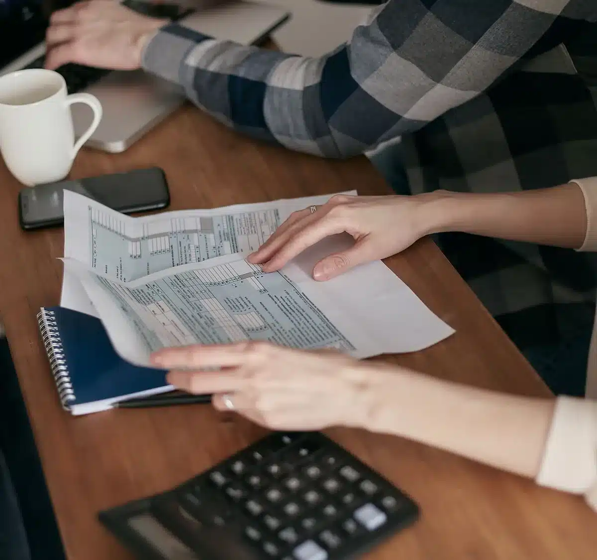 Mains organisant des documents et factures sur un bureau, symbolisant la gestion administrative et l'autonomie financièr